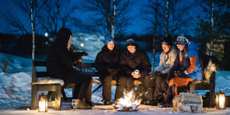 Gruppe sitzt am Lagerfeuer in Schwedisch Lappland
