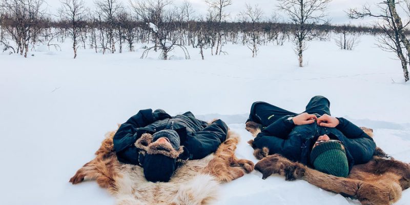 Menschen liegen auf Fellen im Schnee